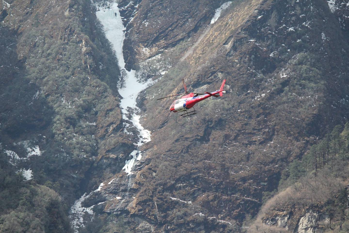 A helicopter flying close along a gorge wall near Namche Bazaar, a frozen waterfall beside it.