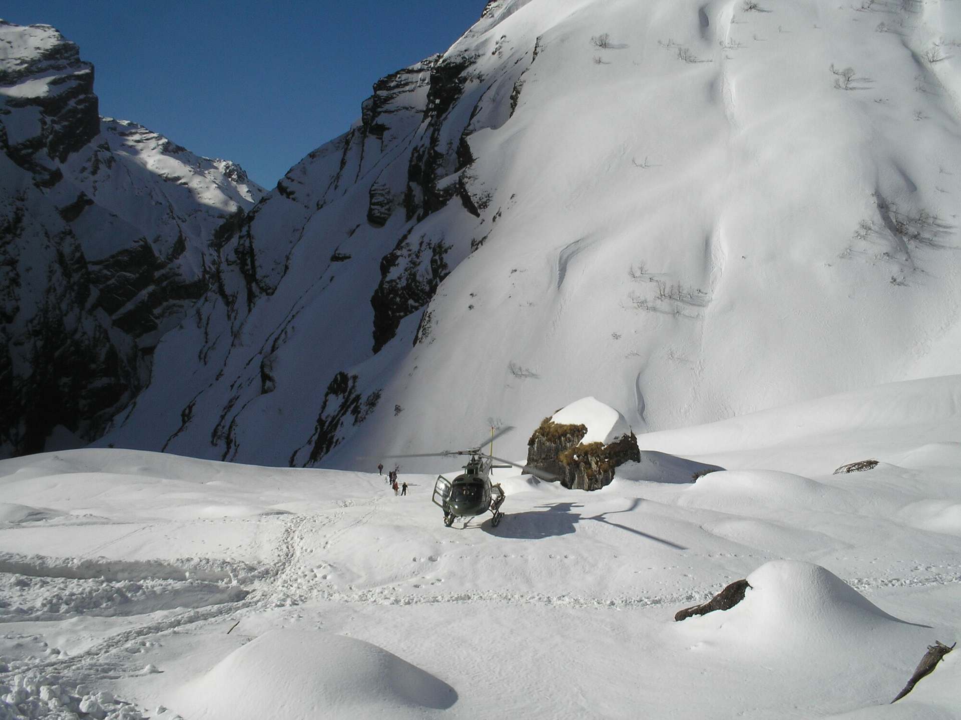 A helicopter standing on a snowfield in the Annapurna region, a wall of rock and ice above it.