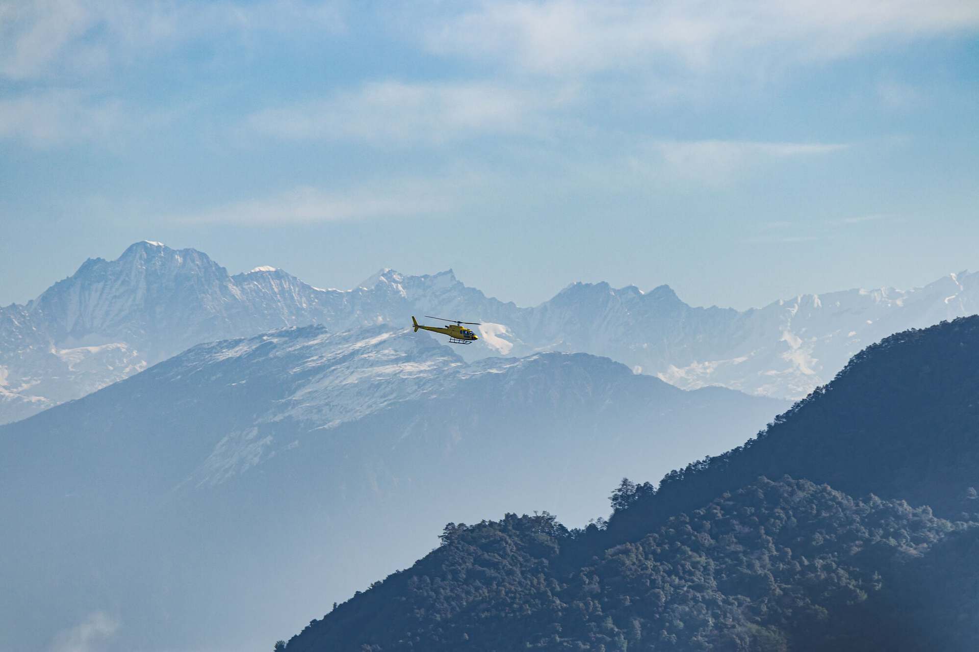 A helicopter crossing the Langtang range on a clear winter morning, ridges layered in haze below.