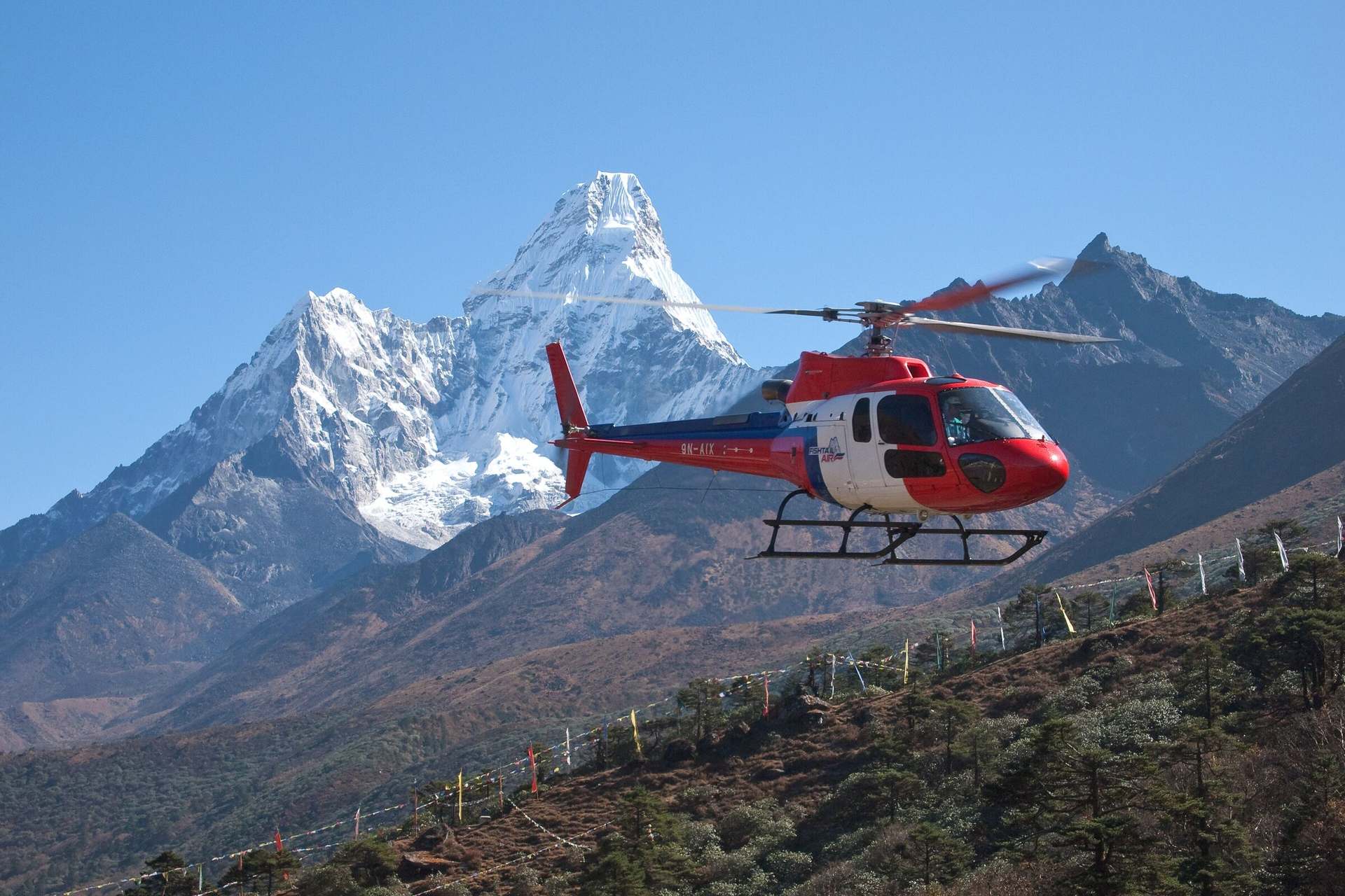 A helicopter in the cruise over the Khumbu with the summit of Ama Dablam rising behind it.