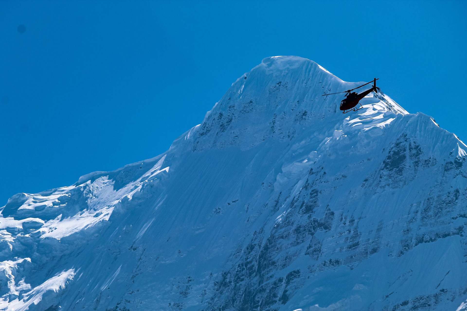 A helicopter dwarfed by the snow and ice face of Nilgiri, the wall above the Kali Gandaki.