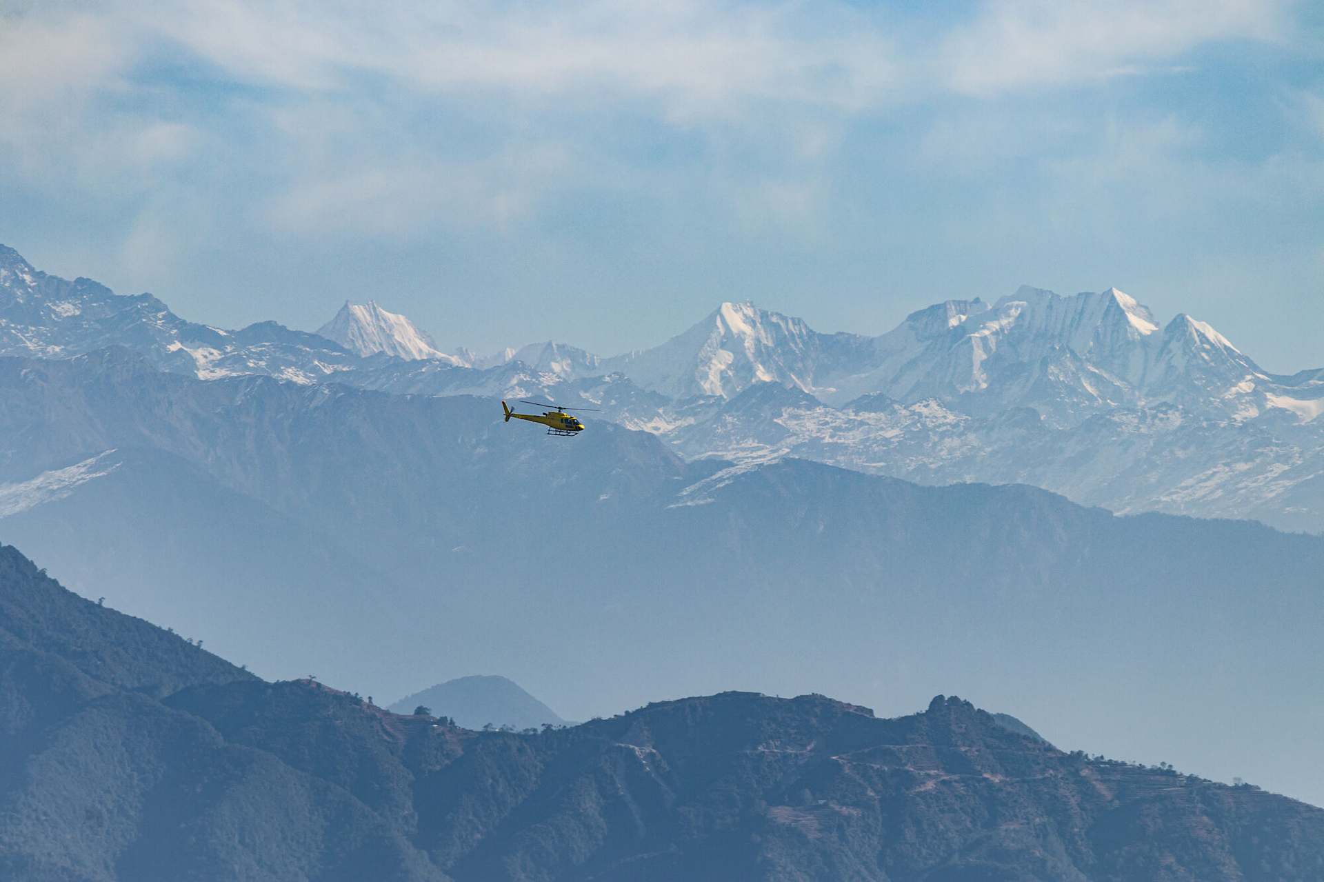 A helicopter returning from a mountain flight over the Langtang range, the snow wall standing behind it.