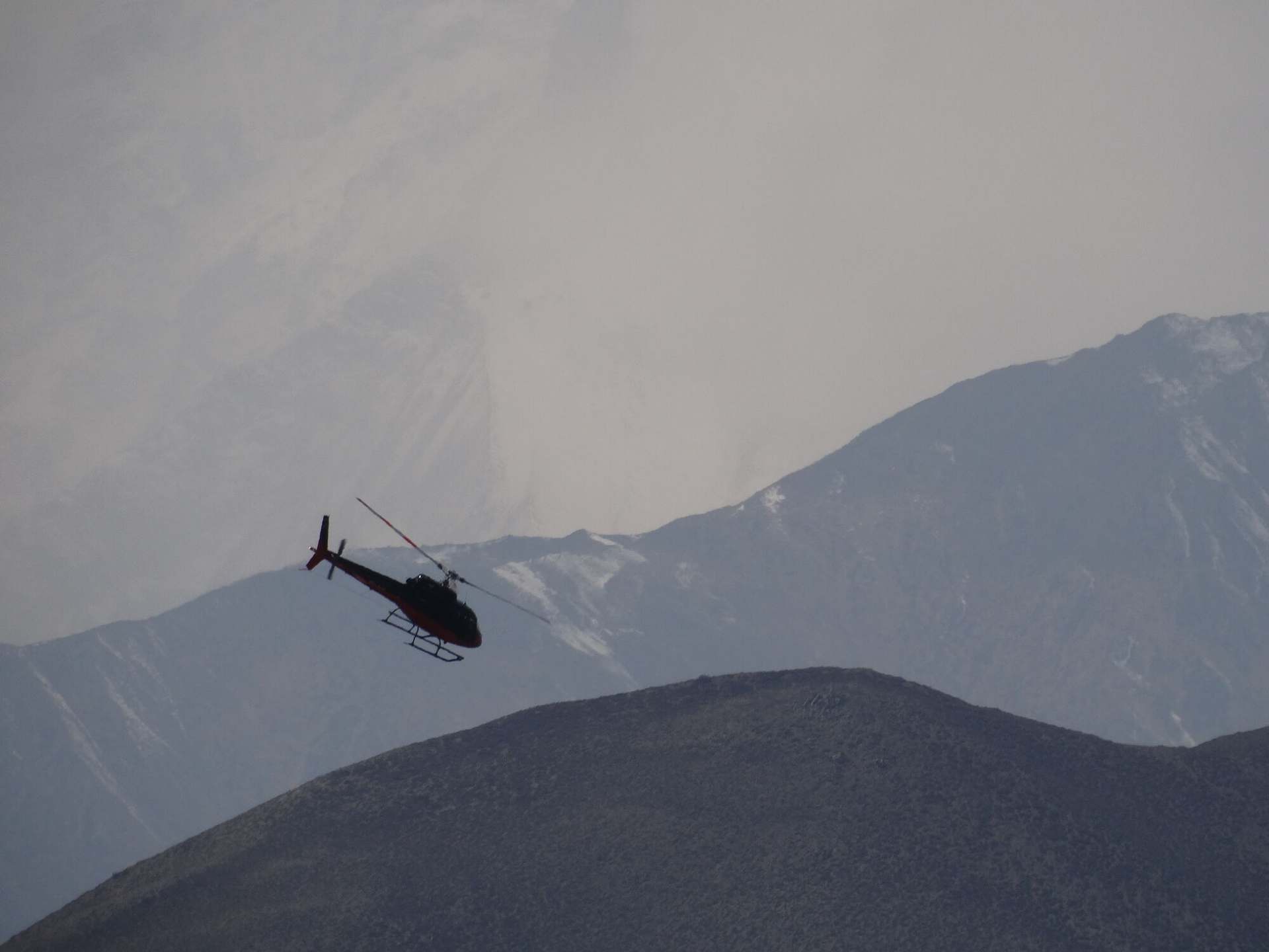 A helicopter in silhouette crossing the bare ridges above Muktinath in Mustang.