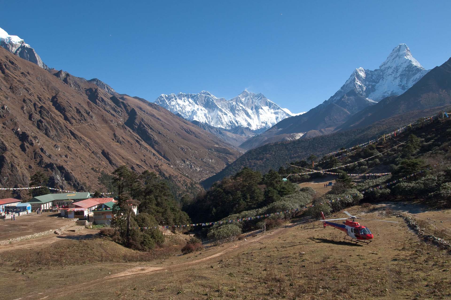 Everest, Lhotse and Ama Dablam over the Imja valley, a helicopter on the ground at Tengboche small beneath them.
