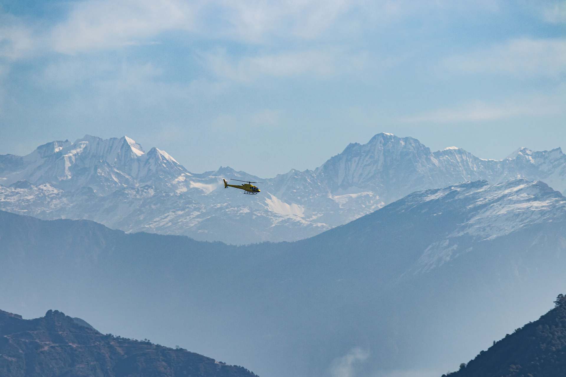 The ground the service covers: a valley of terraces and settlement under the Nepali hills, a helicopter crossing it.