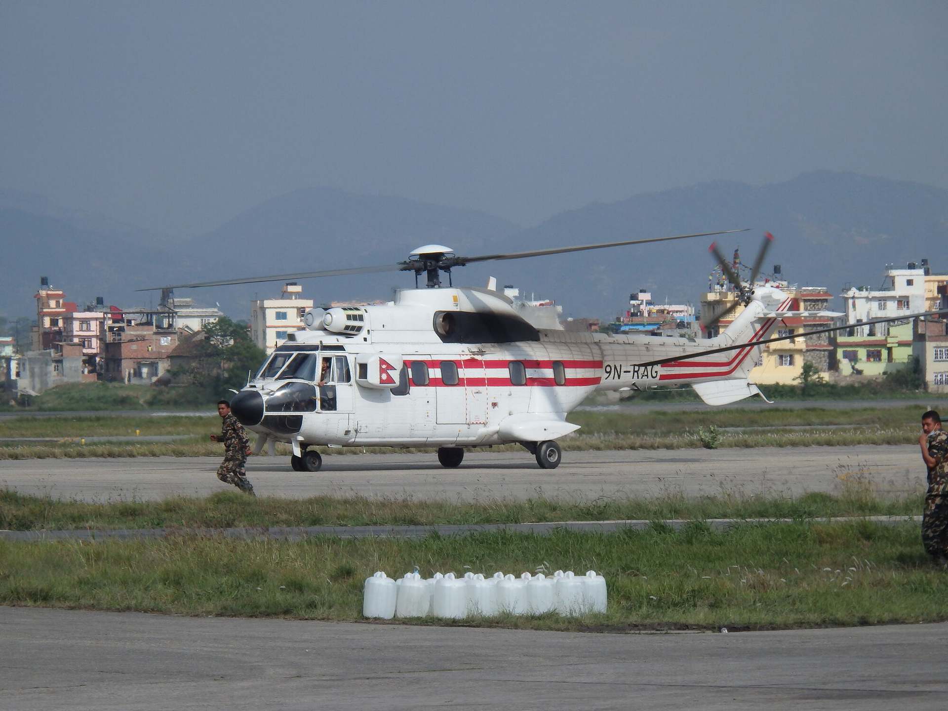 A helicopter standing on the apron at Kathmandu, the city and the hills of the valley behind the airfield.