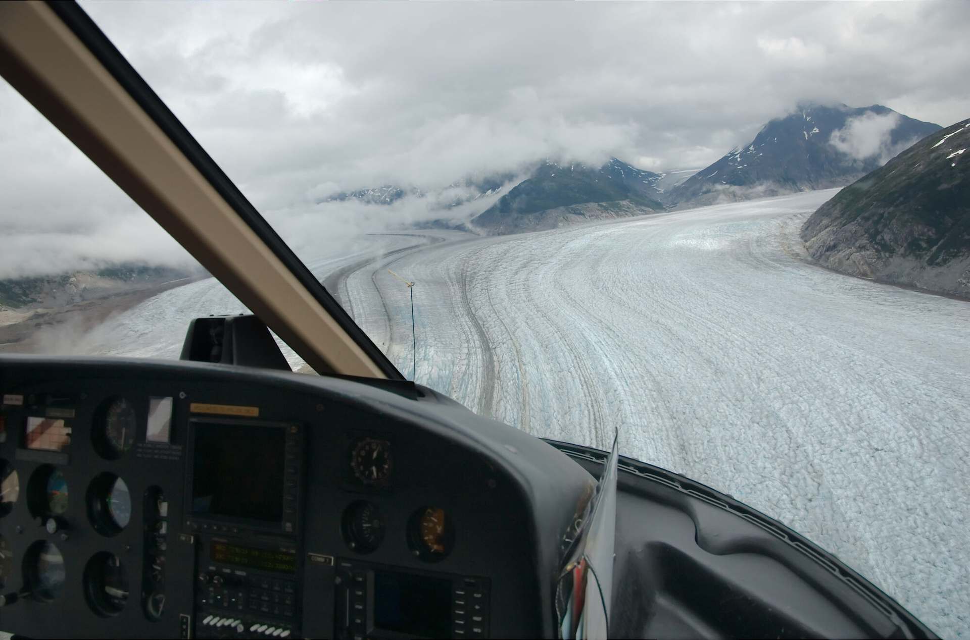 An AS350 cockpit in the cruise, the instrument panel and coaming in the foreground and a glacier running away ahead.