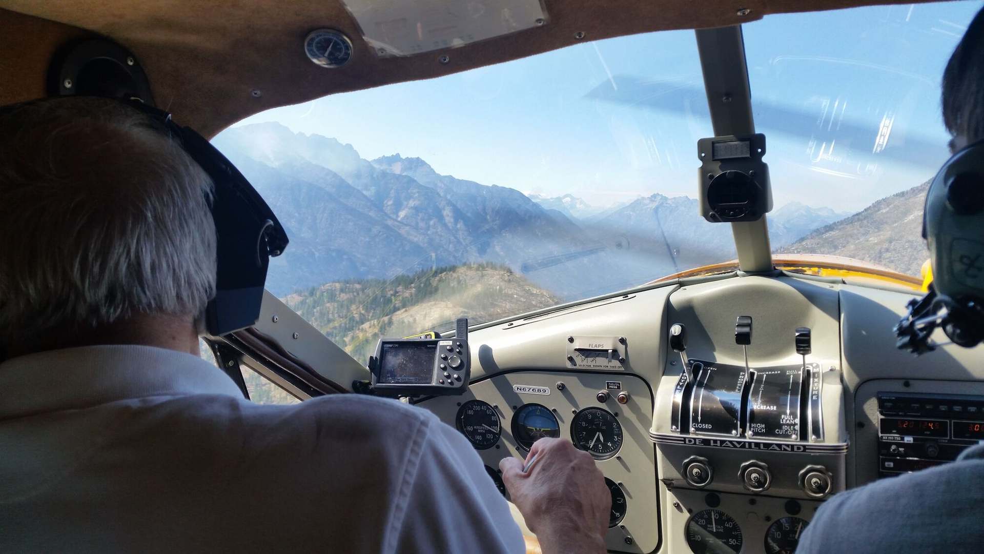 A helicopter cockpit in the cruise, the instrument coaming lit below the windscreen and a ridge line beyond it.