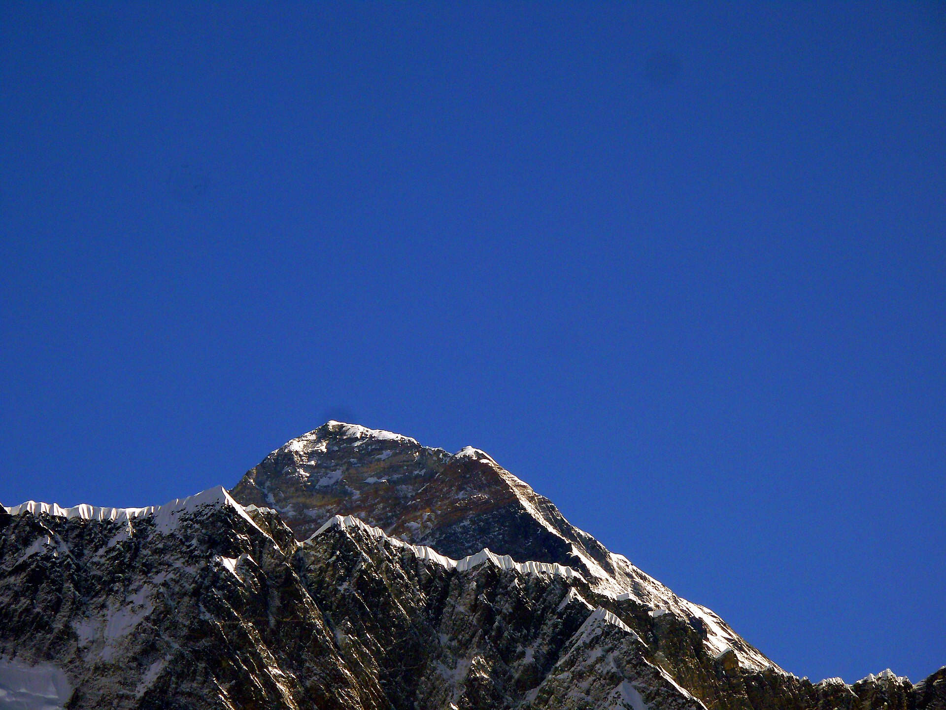 The summit pyramid of Everest and its yellow band of rock, seen close up against a dark blue sky.
