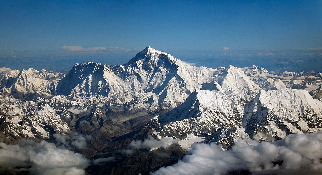 The Everest massif seen from cruise altitude, ridges cutting above a cloud sea.
