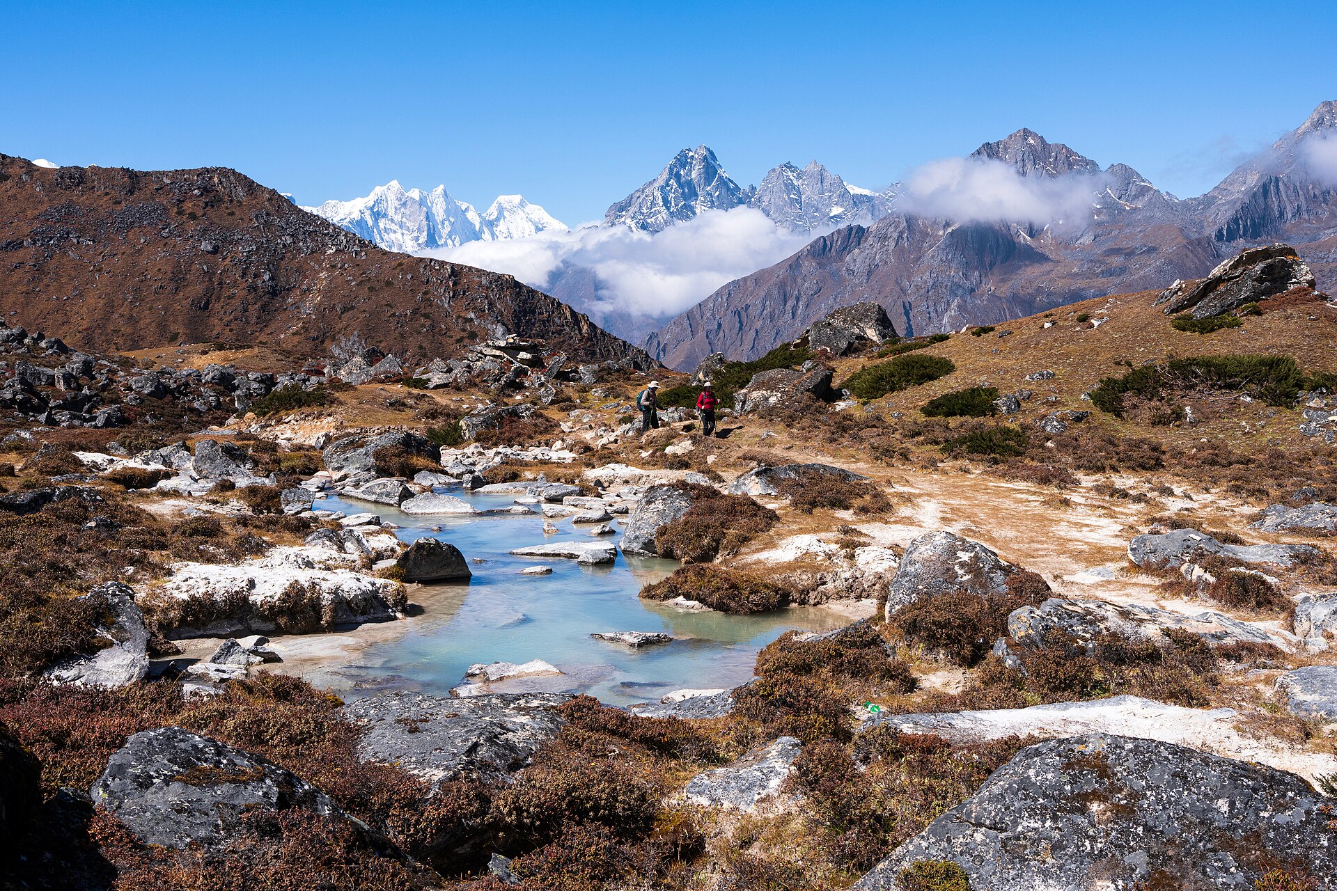 Trekkers on the moraine below Ama Dablam, glacial meltwater pooling in the foreground.